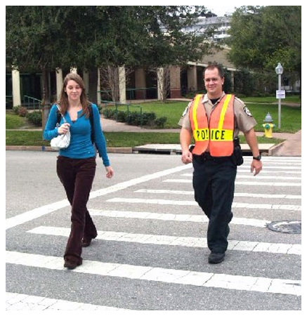 Law enforcement officer and pedestrian crossing the street at a crosswalk.